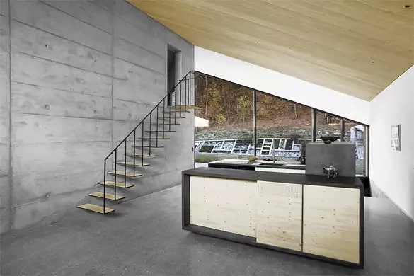 Vue depuis le salon: un seul mur central en béton porte toute la charpente. L'escalier formé de méplat en acier est encastré dans le mur. La cuisine est formé de trois volumes qui organisent le plan en trois sous-espaces: l'entrée (à droite), la
