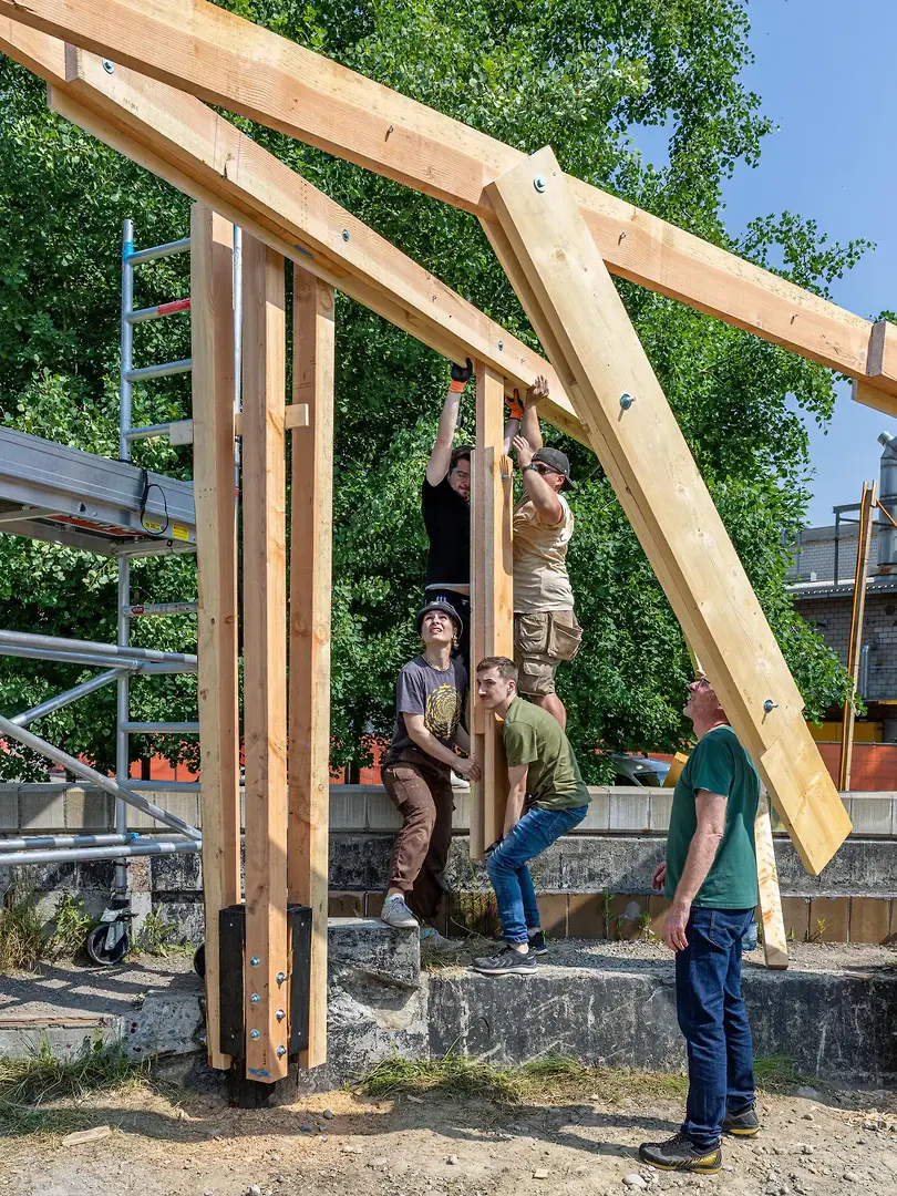 Im Kreis des ehemaligen Klärbeckens der Viscosistadt werden mit Hilfe eines großen Hebelarms überkreuzte und ineinandergreifende Träger in Position gebracht.
