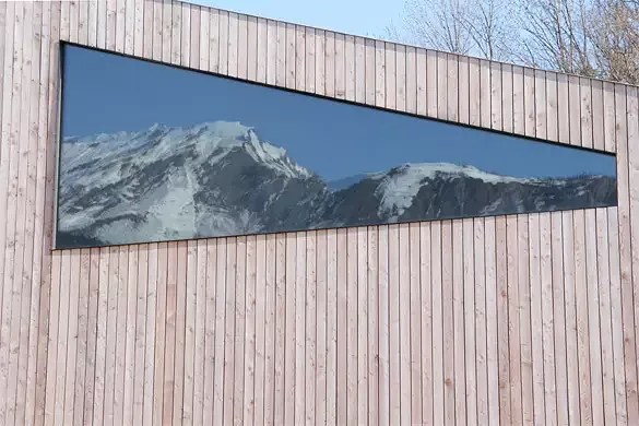 Vue sur la grande baie vitrée qui reflète le massif alpin. Le détail du cadre à été étudié afin de l'affiner au maximum pour le rendre imperceptible.