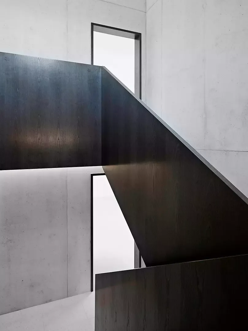 Alle Wände und Treppen der Gemeinschaftsräume sind aus Sichtbeton, während für die Türöffnungen und das Geländer dunkle Esche verwendet wurde. Wie  ein Band entwickelt es  sich nach oben und verbindet alle Etagen.