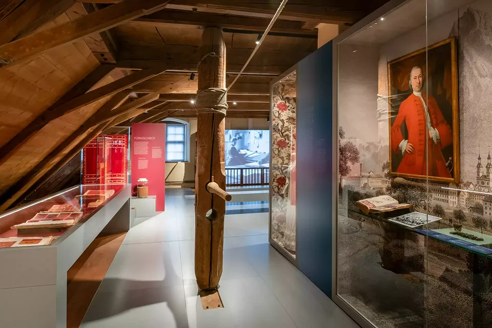 Vitrine avec un tableau de Johann Heinrich Streiff, le fondateur de la première imprimerie textile glaronnaise, ainsi que divers documents et objets datant de l'époque de son activité. A gauche, une vitrine avec des livres d'échantillons.