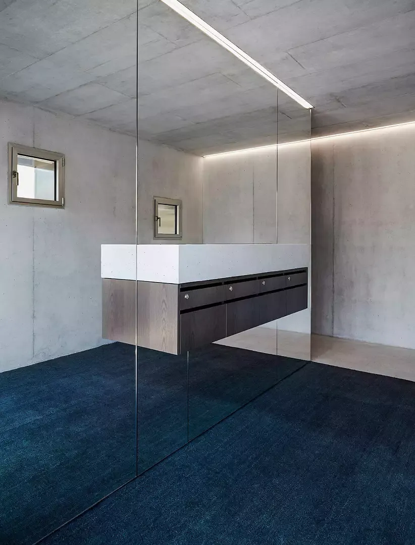 Le grand palier d’entrée est composé d’un grand miroir et d’un grand paillasson gris anthracite.  Un élément en béton au mur sert de soutien aux boîtes aux lettres en frêne teinté foncé.