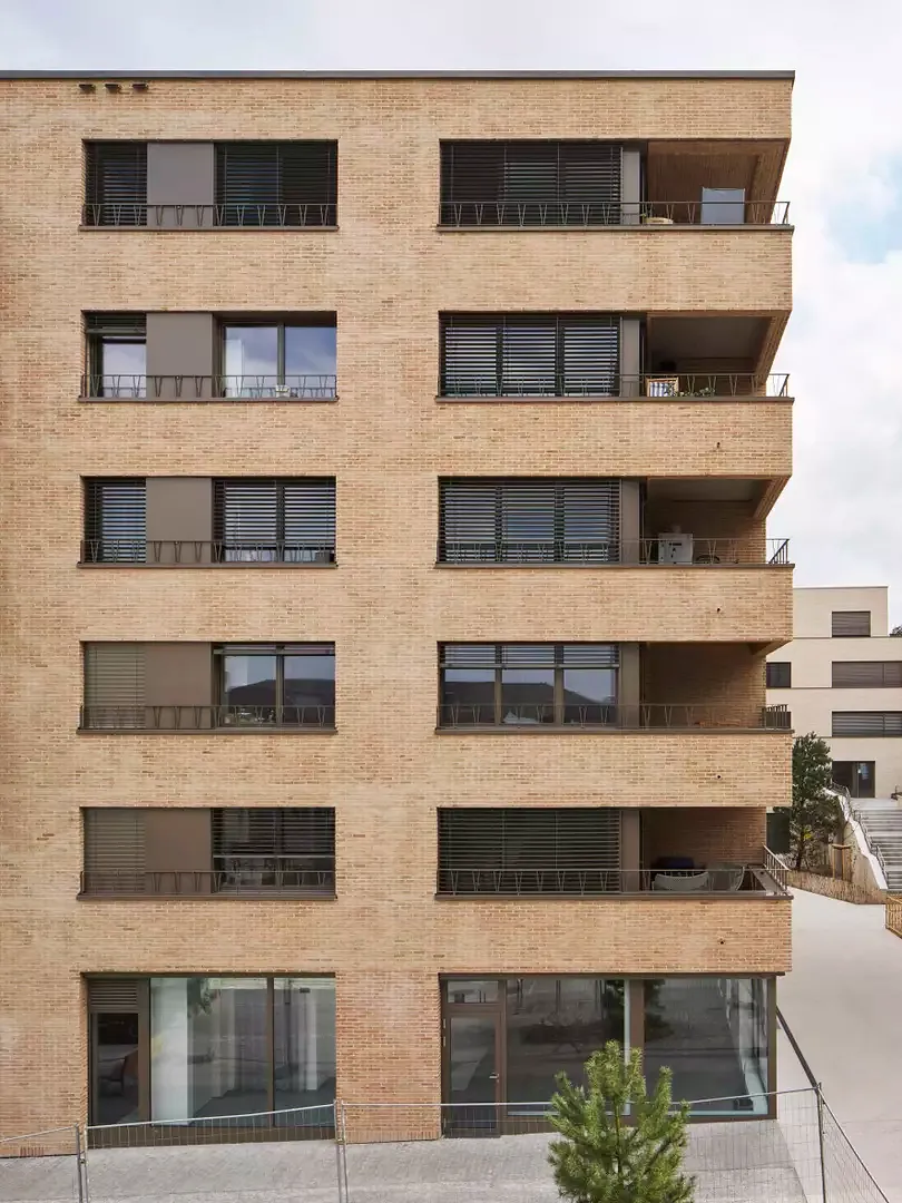 La briquette aux tons rougeâtres enveloppe le bâtiment d’une matière chaleureuse, lui conférant une présence minérale qui transmet à la fois confort et ancrage, tout en dialoguant avec les teintes du quartier. 