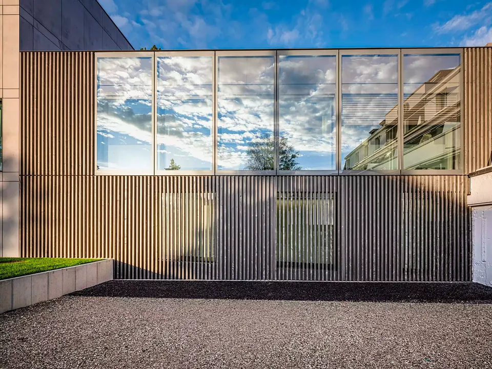 Die Fassade des zweiten Gebäudes besteht aus  einer Holzverkleidung und lichtdurchlässigem Glas.  Das Gebäude erscheint  durch die Kombination  dieser beiden Materialien leicht und zeitgeistig.