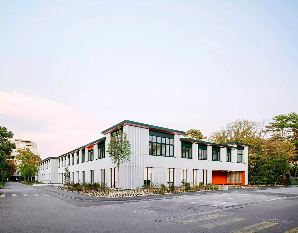 Blick auf die südwestliche Fassade mit dem eingezogenen Eingangsbereich zur Wilhelm-Klein-Strasse. Ganz in Ziegelrot eingetaucht, bietet er Schutz und Geborgenheit.