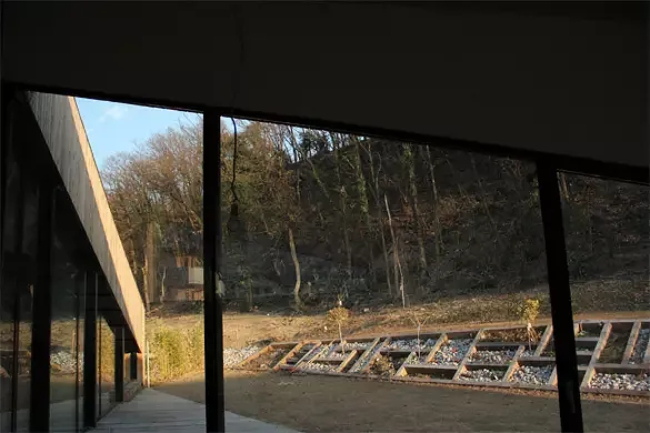 Vue depuis la salle à manger: le jardin et la forêt sont en continuité de l'espace intérieur. La différence de niveau entre les deux terrasses est assuré par une série de cadres en mélèze ayant pour fonction de retenir la terre et de former un