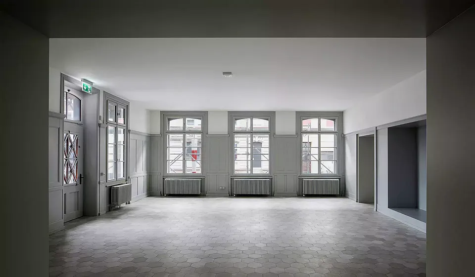 Vue du le rez-de-chaussée de l’ancien bâtiment, rénové avec sensibilité, qui sert actuellement d’espace de coworking.  Une des particularités: les nouveaux carreaux de céramique hexagonaux de couleur grise.