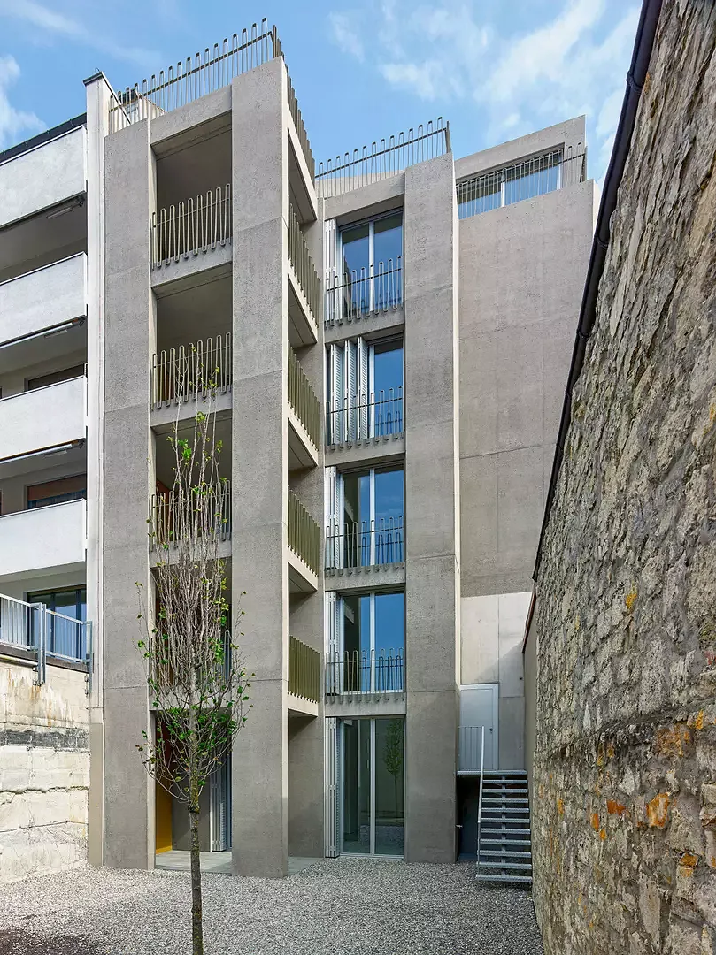 Vue de la petite cour sur la  façade arrière: conçus à partir  des mêmes matériaux que ceux utilisés côté rue, les éléments porteurs en béton décapés à l’eau et les garde-corps, qui encadrent les balcons couverts.