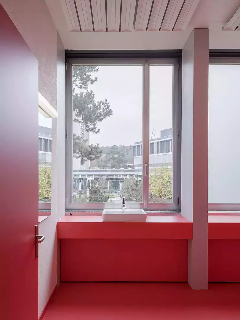 HPT Bioturm, aile des ateliers – sanitaires avec accents rouge fraise et vue sur l’espace vert