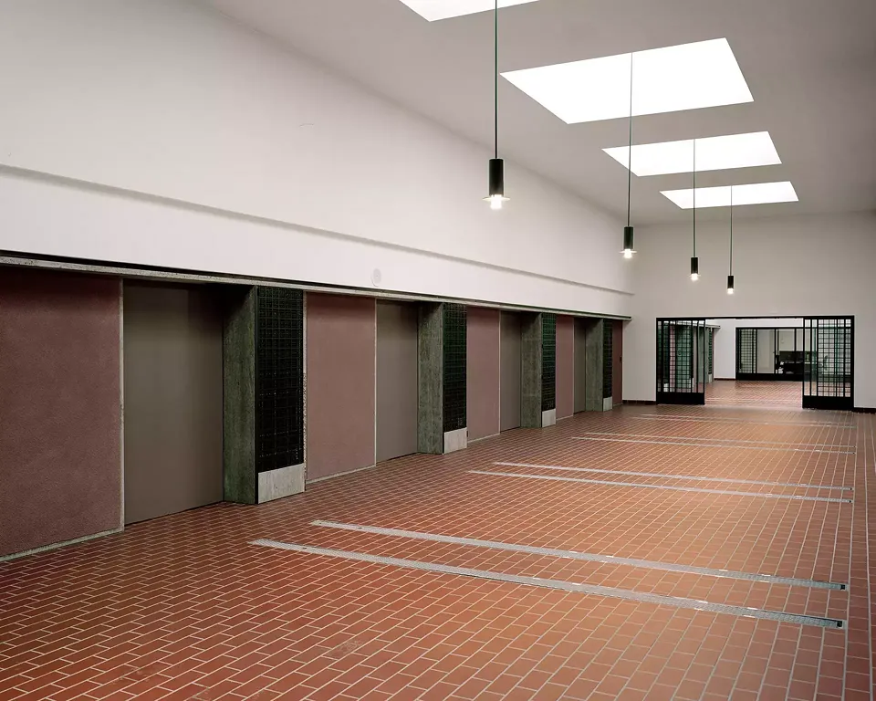 Die Ofenhalle mit den automatischen Schiebetüren und Lüftungsgittern. Muschelkalk, Zunderstahl, Messing, Caput Mortum. Die Leuchten sind eine Abwandlung der bestehenden Leuchten in der Kapellen.