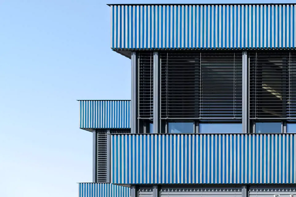 Die Architekten orientierten  sich bei der Farbwahl der Fassadenverkleidung an die Farbpalette des Sees und der nah gelegenen Weinberge. Von einer Seite wirkt die Fassade Blau, von  der anderen Seite Grün – so entsteht ein Farbspiel je nach Blickwinkel.
