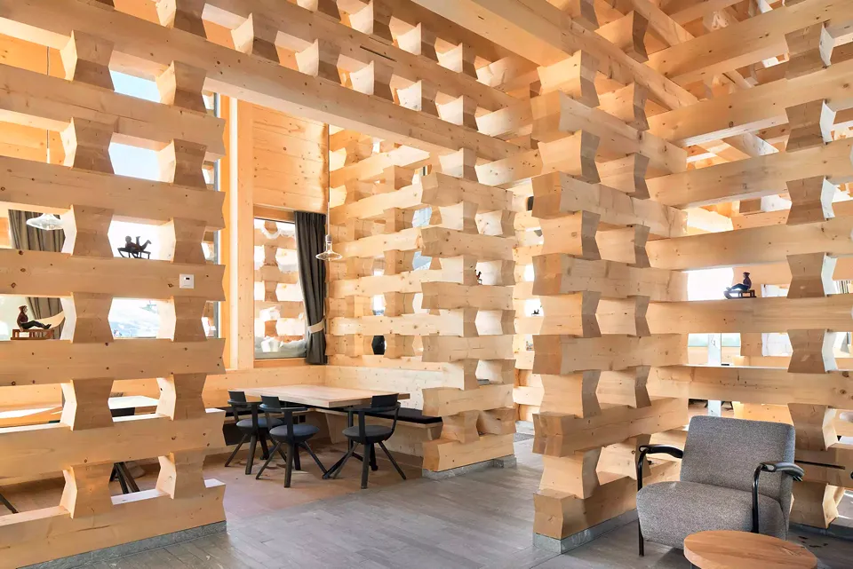 Holz wohin das Auge reicht. Die tragenden Innenwände lassen durch die offene Konstruktion das Sonnenlicht in die  Hütte strömen und gewähren den  Gästen den Durchblick.