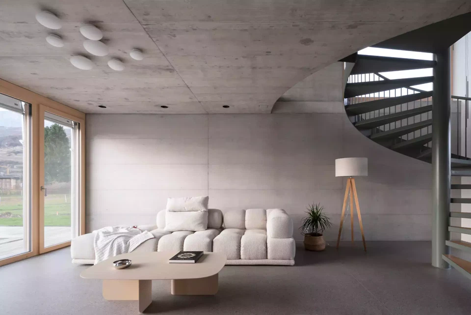 Eine zurückgesetzte grüne Wendeltreppe im Wohnzimmer, zwischen Sichtbeton und gewachstem Estrich