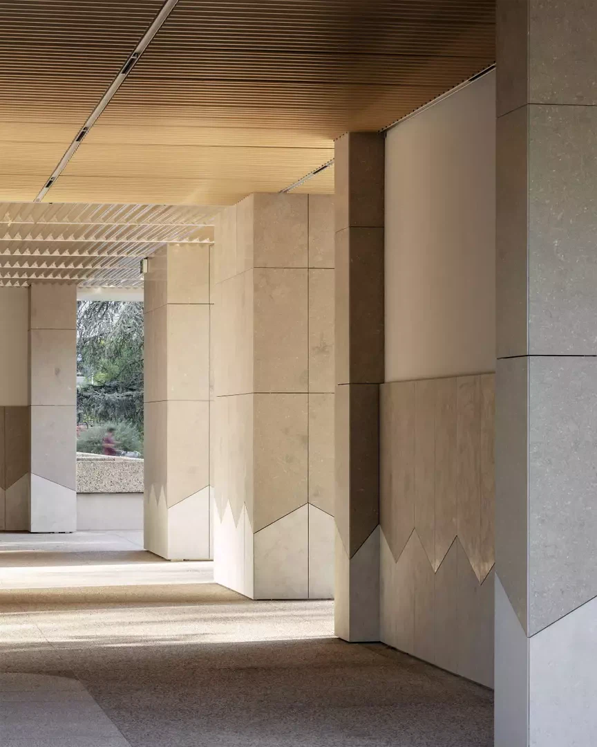 Mit beigen Natursteinplatten wird das Erdgeschoss als Sockel artikuliert, der als öffentlicher Bereich zwischen Innen- und Aussenraum vermittelt.