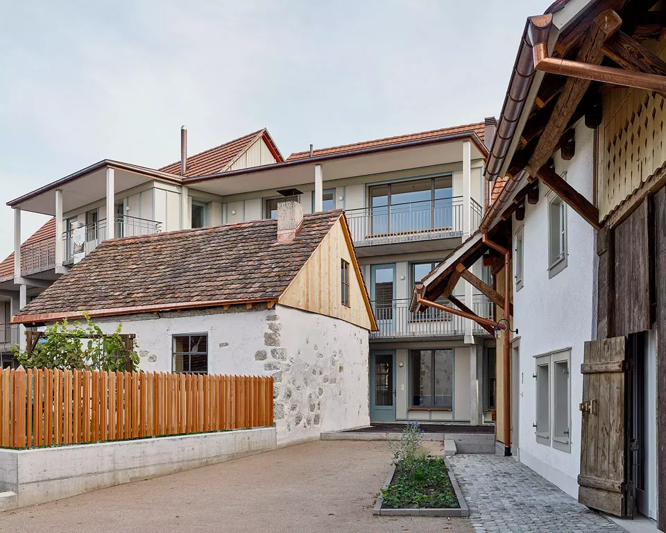 Vue sur la construction neuve avec de grandes ouvertures de  fenêtres et une large coursive orientée nord. Au premier plan, l'ancien Schmitti, et à droite les façades d'entrée des deux Taunerhäuser.