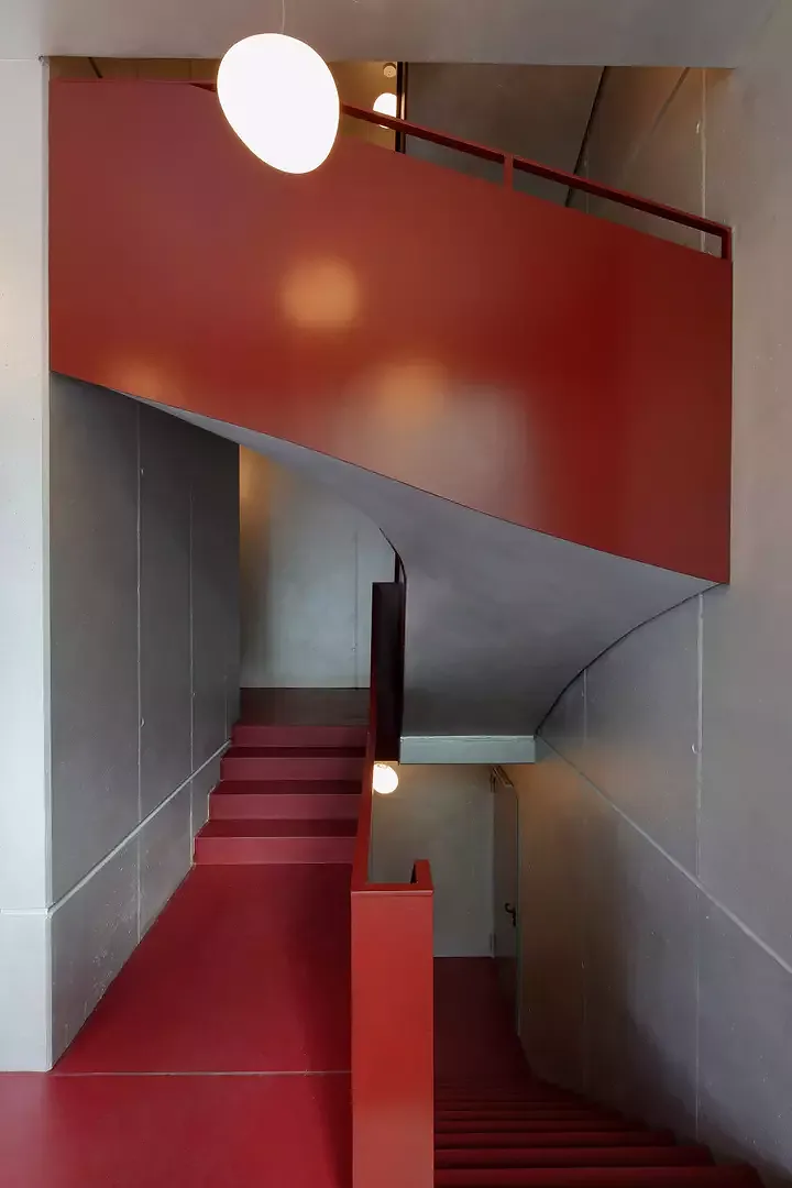 Treppenhaus Bernhardstrasse. Das Bordeauxrot der geschlossenen Treppenhausgeländer kontrastiert mit den silbernfarben angelegten Sichtbetonflächen.