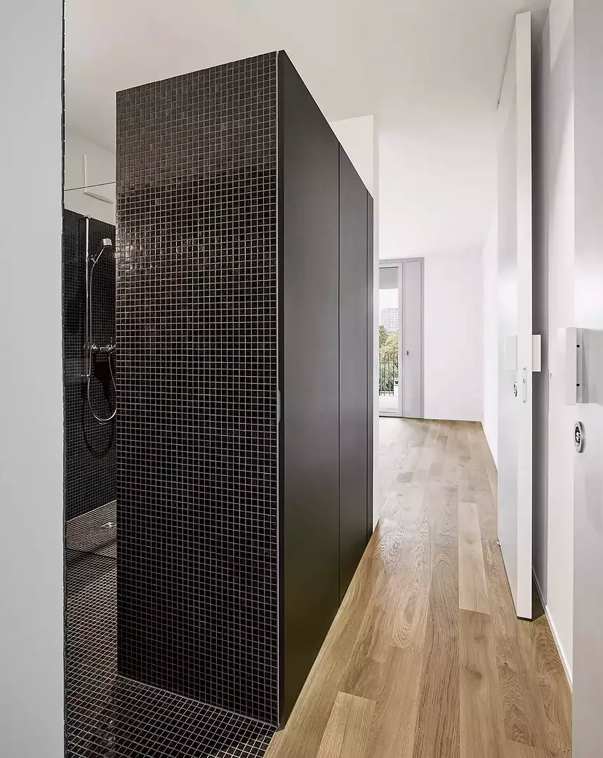 Die nördliche Schicht des Grundrisses mit der mittigen,  mit dunklen Mosaikfliesen ausgekleideten Nasszelle, die  ihn in zwei gleichwertige Räume teilt. Das Badezimmer ist  bei Bedarf von zwei Seiten mit einer Pivottür zu schliessen
