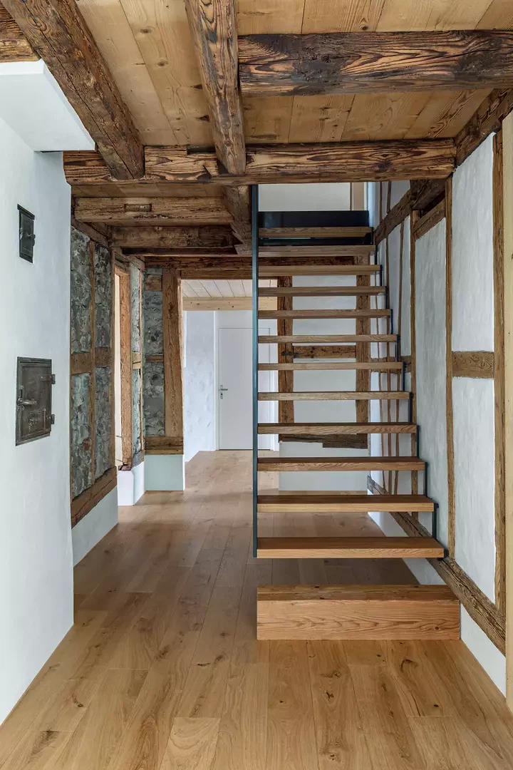 Neue Stahltreppe im Bestand, freiliegendes Holzriegelwerk und historische Balkendecke.