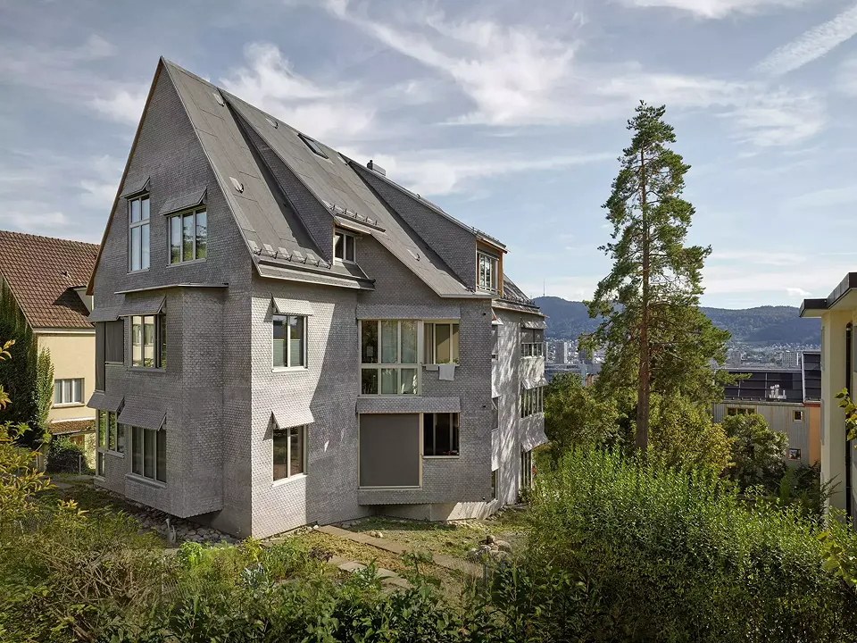 Sur les pentes de Zurich-Höngg, la fondation PWG a érigé un immeuble d'habitation qui tord et brouille les lois de la construction en une forme loufoque aux espaces intérieurs en expansion.