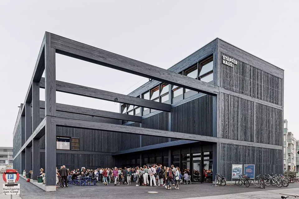 Direkt gegenüber des Bahnhofs  strahlt dervorfabrizierte und in 3D geplante Holzbau mit der einladenden  Pergola Leichtigkeit und Offenheit aus. Das disponible Raumgitter zieht die  Besucher förmlich in seine nachtblaue Gebäudehülle hinein.