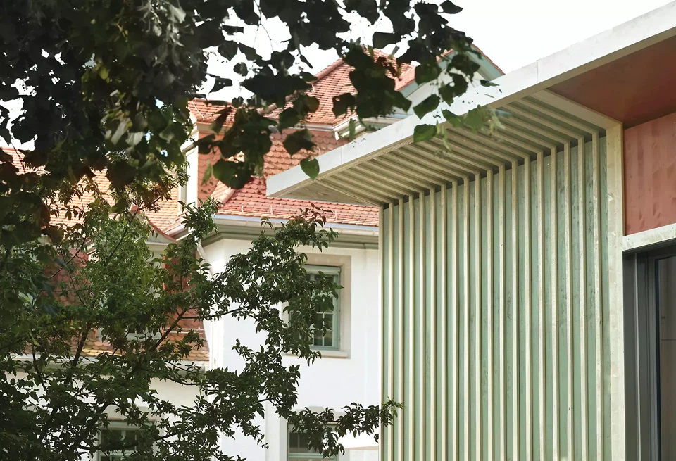 Die Holzfassade des Pavillons setzt die Materialität der Bestandsbauten fort und fügt sich mit Farbe und Struktur harmonisch in die natürliche Umgebung ein – Blickrichtung «Tilia Wohnen und Beschäftigung»