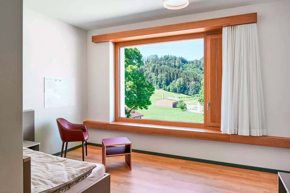 Die Fenster der Patientenzimmer sind  in Eiche ausgeführt  und mit grosszügigen, tiefliegenden Brüstungen ausgestattet, um auch  als Sitzbank zu dienen.