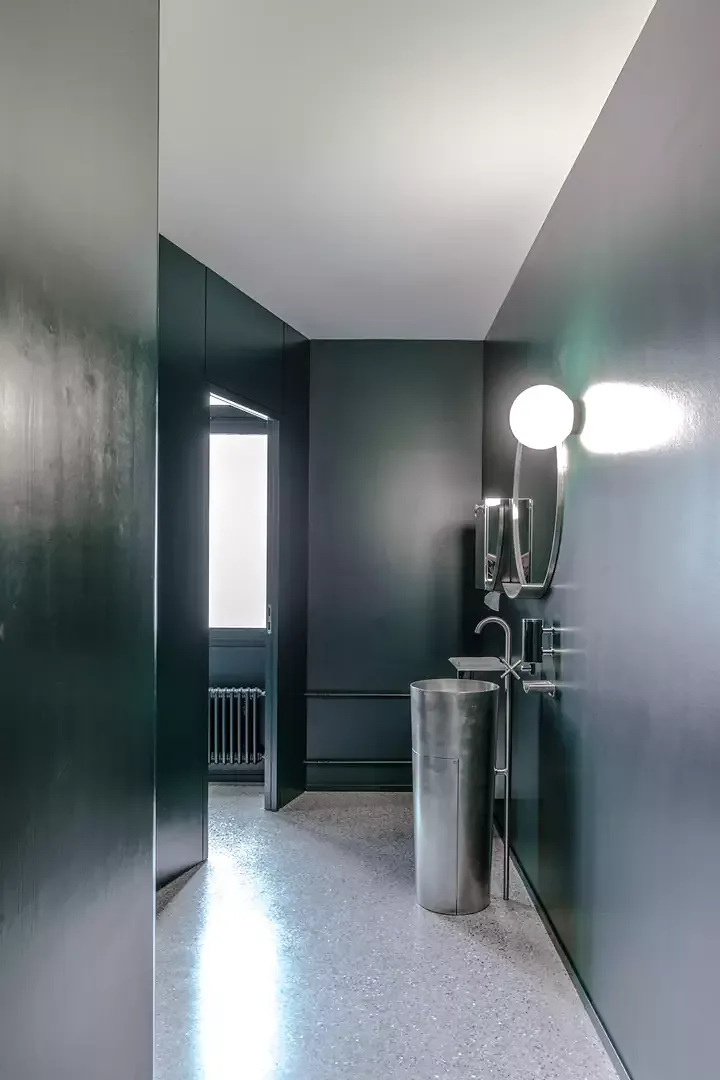 Vue du vestibule des toilettes avec une fontaine en acier inoxydable, un nouveau  sol en terrazzo et des surfaces murales vert foncé.
