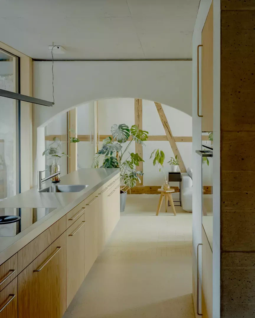 Die Küchenzeile greift in den Tennraum, während der Bodenbelag den Übergang subtil akzentuiert.