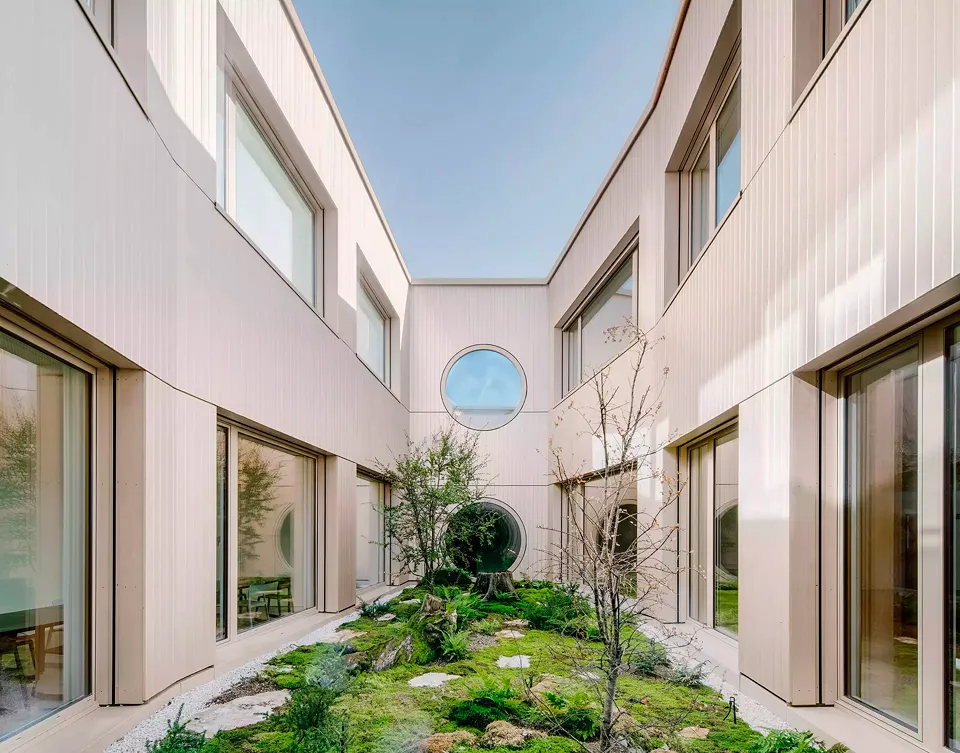 Blick in den polygonalen Innenhof, der mit seiner bemoosten Bodenfläche, Steinen und Bepflanzung japanisch anmutet. Zahlreiche grosse Fensteröffnungen und Bullaugen orientieren sich zu diesem intimen Innenhof.