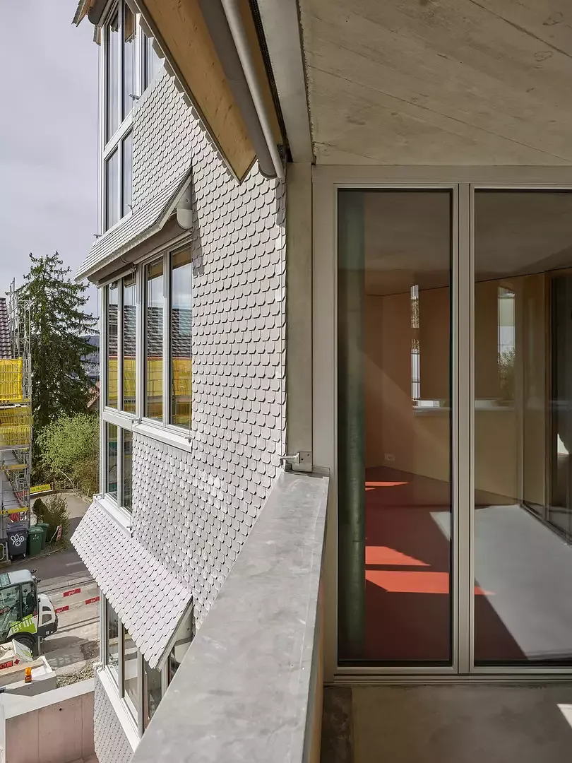 Le revêtement de la façade en écailles d'Eternit reflète la géométrie à petite échelle et habille le corps du bâtiment d'une robe légère. Cette impression est renforcée par les fenêtres ouvrant sur l'extérieur et les toits de stores évasés.