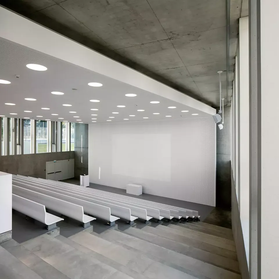 Le minimalisme en  termes de matériaux s’exprime particulièrement bien dans l’aula. Le plafond acoustique se prolonge  sur le mur et devient une surface de projection.