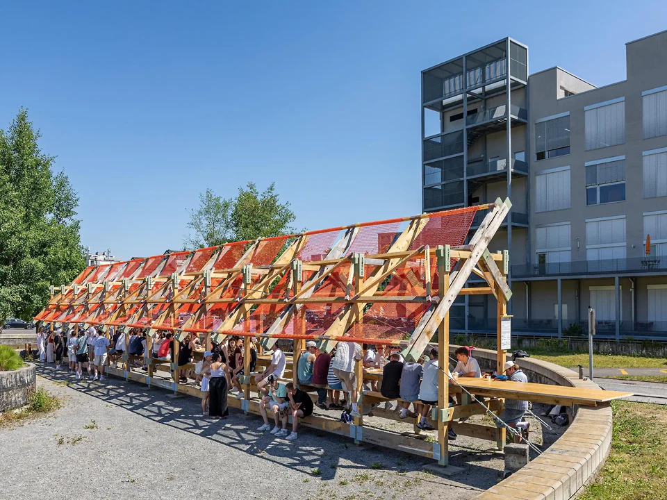 Zwischen Holztragwerk, rotem Netz. und bestehendem Beton entsteht im ehemaligen Klärbecken ein temporärer Ort des Zusammenkommens