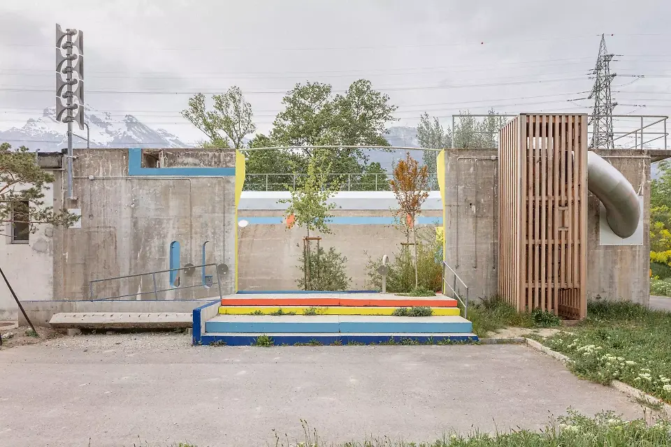 Vue sur l'entrée de la facade sud. Une tour et un toboggan permettent aux enfants de traverser le mur. Les escaliers du 1 er plan sont composés des pans de béton découpés et recyclés. 