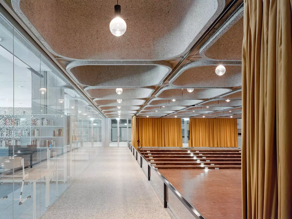 Die Aula mit Terrazzoböden und akustisch wirksamen Sichtbetonfertigteilen