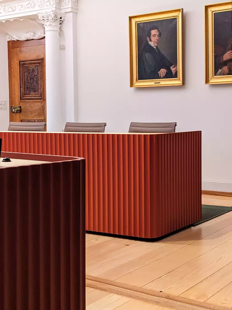 der Konferenztisch in Rot mit seiner Kanellierung und den gerundeten Ecken interpretiert die reichhaltige Ausgestaltung des Bestands