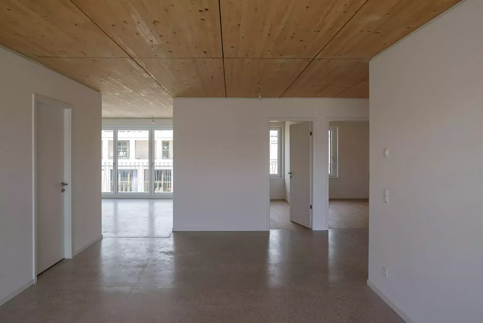 Tous les appartements adoptent des typologies traversantes, offrant une grande qualité de lumière naturelle. Au plafond, la structure en bois apparent rappelle le système constructif et l’engagement durable du projet.