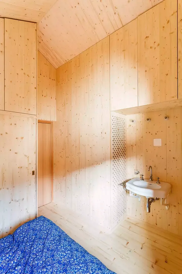 La grande chambre de l’étage fait une utilisation de l’espace optimisée. Les rangements sont intégrés dans les murs, alors qu’un panneau aux motifs découpés à la CNC dissimule un radiateur placé dans la niche d’un lavabo réutilisé.