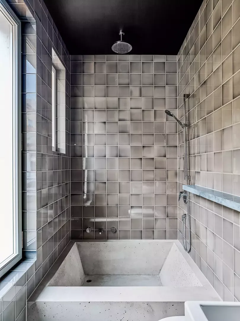 les carreaux de salle  de bain du fournisseur «Golem» brillent de reflets nacrées grâce  à leur structure de glacis craquelé. La baignoire à mi-hauteur, coulée dans du béton sur place, a été rendue hydrophobe.