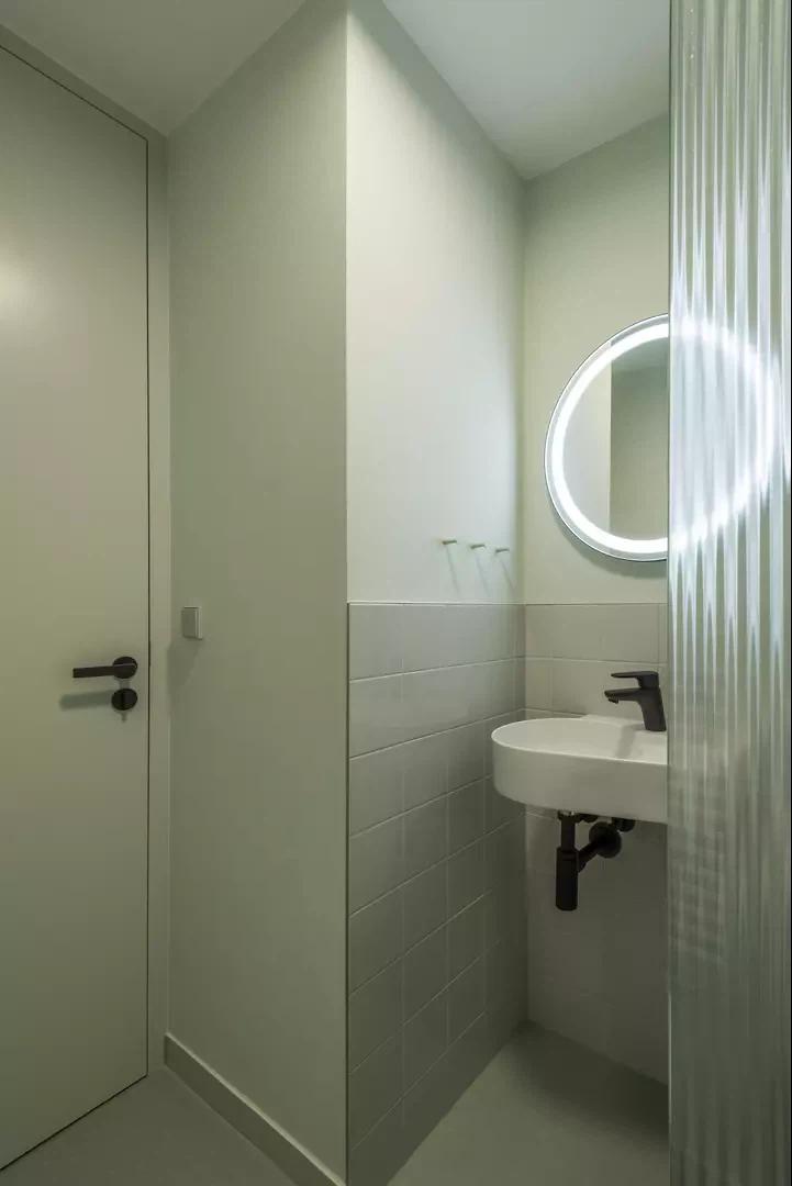 Minimalistisches Badezimmer mit hellgrünen Oberflächen und schwarz-weisser Ausstattung.