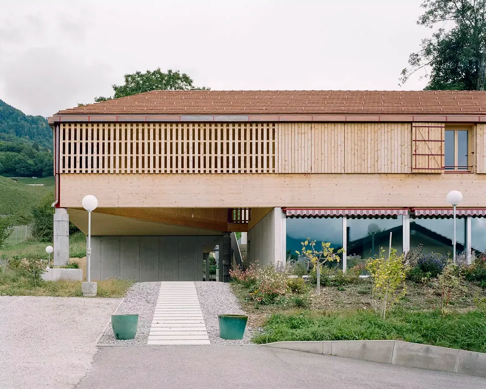 La façade en bois, dont  les ferblanteries de couleur rouge foncé rapellent la maison existante, fait référence au côté rural du hameau de Villy. L’aménagement extérieur se veut simple, naturel et ouvert, contrastant avec les haies des villas traditionnel