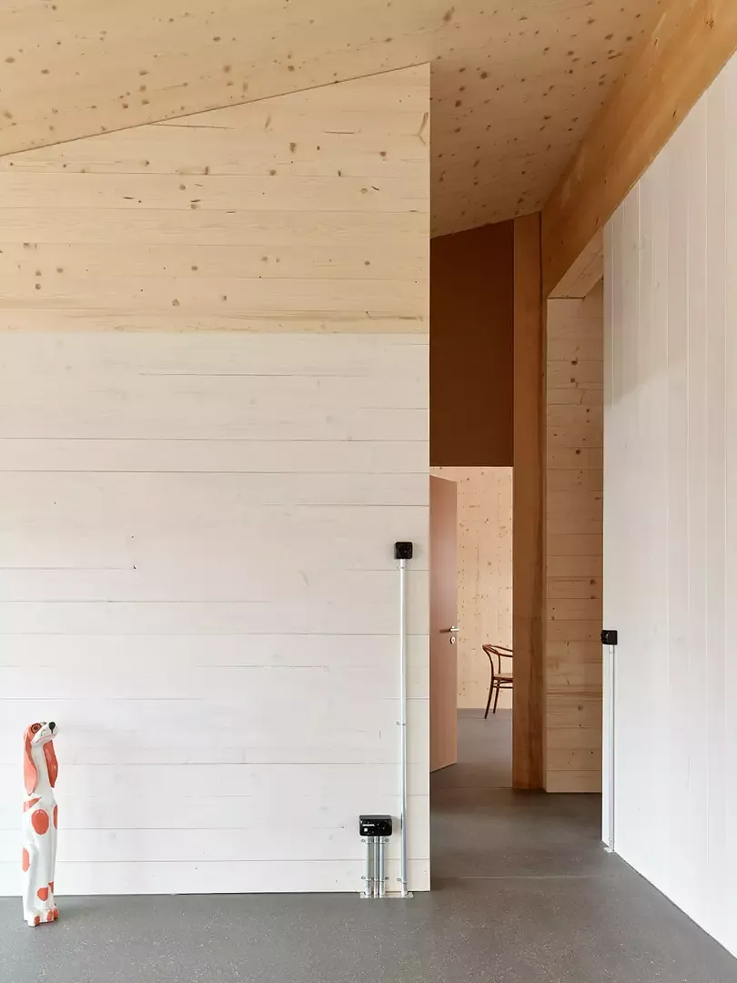 Blick entlang der mächtigen Firstpfette zu den Schlafzimmern in der Dachgeschosswohnung. Die Wohnzimmer werden über gewisse Wandflächen durch eine weisse Lasur entmaterialisiert.