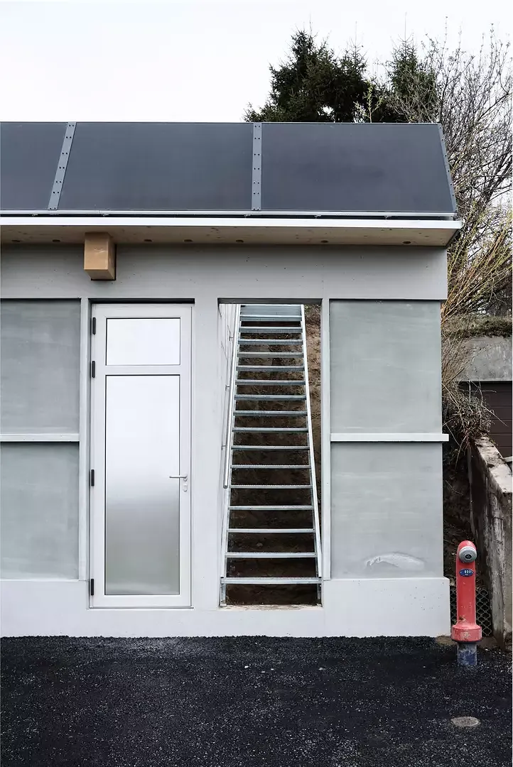 Un accès à la maison située  en dessus a été intégré au nouveau volume. Implanté directement au bord de  la route, le garage agit également comme «portail d’entrée» sur la parcelle.