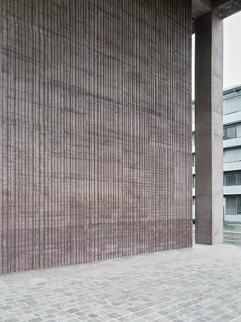 Construction hybride: un socle de 11 mètres de haut en béton teinté en rouge et en pisé confère un caractère chaleureux à l’entrée.