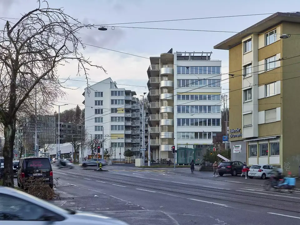 Une petite place de quartier triangulaire agrémentée d’arbres a été aménagée au croisement de la Hofwiesenstrasse et de la Wehntalerstrasse. Située de l’autre côté de plain-pied, l’école enfantine jouit d’une situation plus calme en deuxième front.