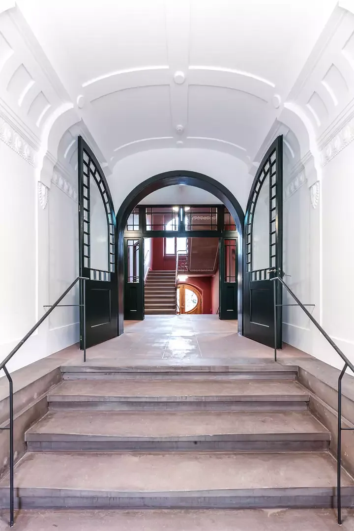 L’entrée avec les portes battantes peintes en  vert foncé, parachevées d’éléments en stuc de  style Art nouveau. Des  mains courantes raffinées  en acier brut huilé se  marient parfaitement aux marches en pierre.