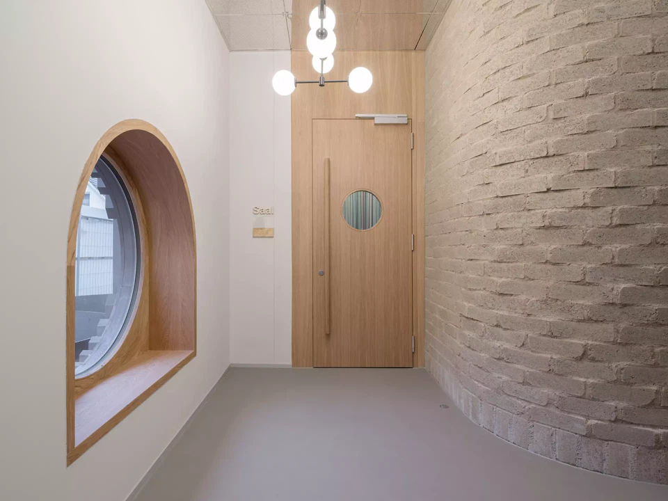 Eingangsbereich mit Blick auf die geschwungene Lehmsteinwand und Zugang zum Foyer.