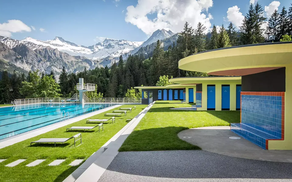 Wiederhergestelltes 50-Meter Schwimmbecken mit neuem Sprungturm und Garderobentrakt vor Bergpanorama
