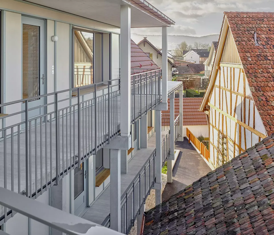 Der grosszügige Laubengang mit Sitzbank in der grossen Fensternische neben dem Wohnungseingang. Rechts die Giebelseite der Taunerhäuser.