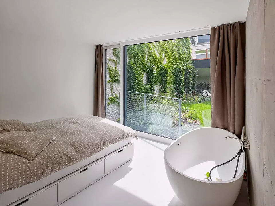Le patio lumineux apporte  à la fois lumière et verdure aux espaces domestiques situés sous le jardin. Le grillage sur lequel pousse la vigne vierge  se transforme en garde-corps  au niveau du jardin.
