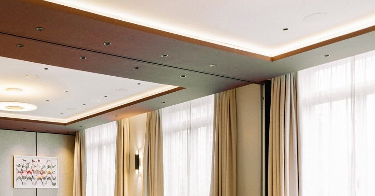 De discrètes corniches lumineuses à intensité variable se fondent sans transition dans le plafond climatiquement actif et accentuent les frises sombres du plafond, les diffuseurs à grille à haute induction avec perforations SonoPerf restent imperceptiblement reconnaissables directement dans le champ de vision des corniches lumineuses. | Photo © monoplan De discrètes corniches lumineuses à intensité variable se fondent sans transition dans le plafond climatiquement actif et accentuent les frises sombres du plafond, les diffuseurs à grille à haute induction avec perforations SonoPerf restent imperceptiblement reconnaissables directement dans le champ de vision des corniches lumineuses. | Photo © monoplan